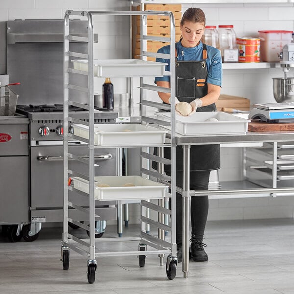 A woman in a professional kitchen using a Regency end load pizza dough box rack.