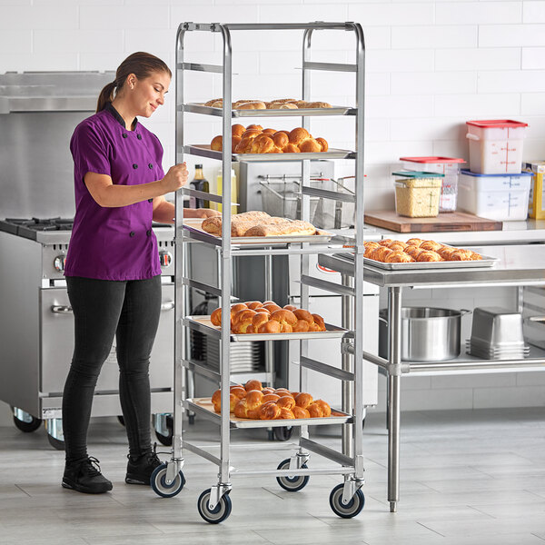 A woman in a purple shirt standing next to a metal rack with trays of food.