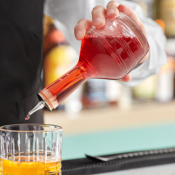 A hand pouring red liquid into a Barfly glass bitters bottle.