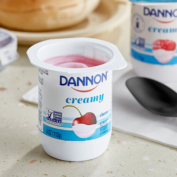 A close up of a container of Dannon Creamy Cherry Yogurt with a spoon inside.