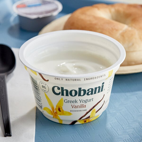 A white Chobani Non-Fat Vanilla Greek yogurt container on a plate with a bagel.