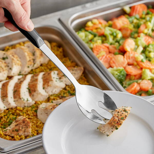 A hand using a Vollrath stainless steel spoon with a black handle to serve food