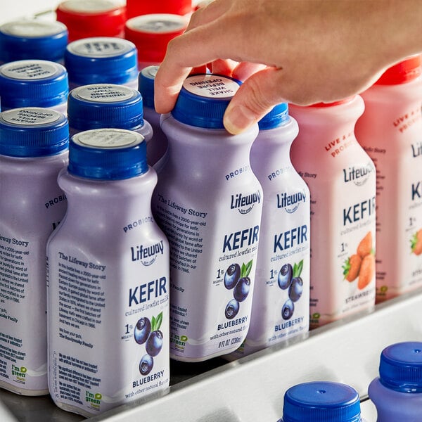 A person's hand picking up a white Lifeway Low-Fat Blueberry Kefir bottle with a blue cap.