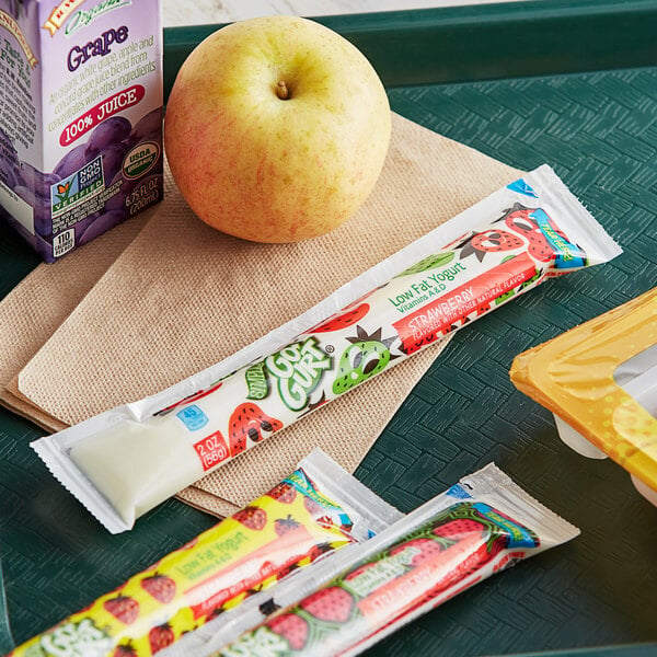 A tray with Go-GURT, a yellow apple, and juice on a table.