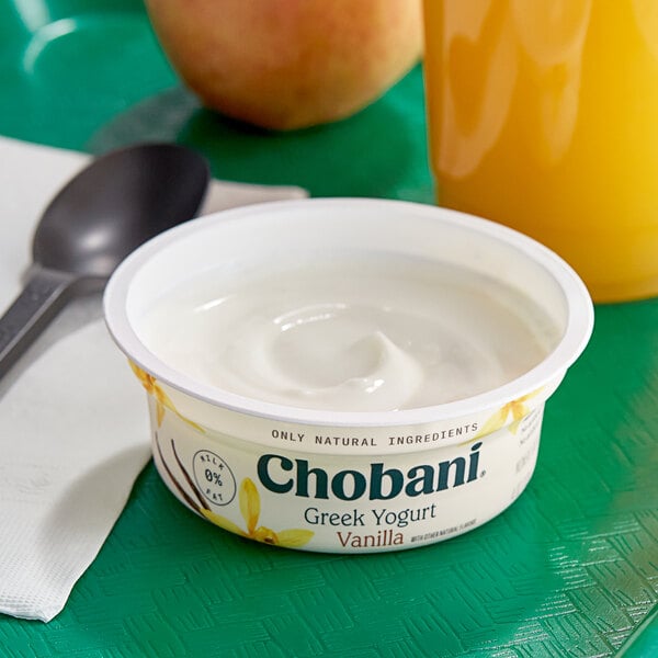 A bowl of Chobani Non-Fat Vanilla Greek Yogurt with a spoon and a glass of orange juice.