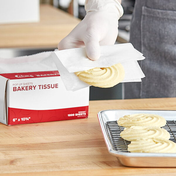 A person in gloves using Choice customizable bakery tissue to take a cookie off a baking tray.