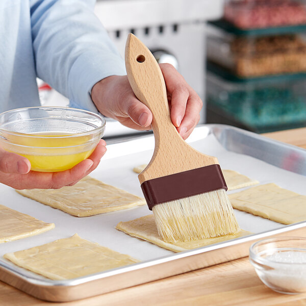 A person using a Vollrath Boar Bristle Pastry Brush to brush dough.