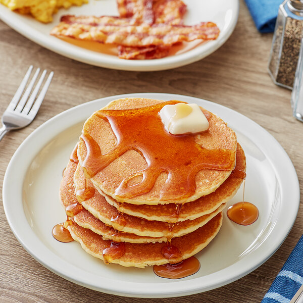 A stack of Krusteaz buttermilk pancakes with butter and syrup on a plate.