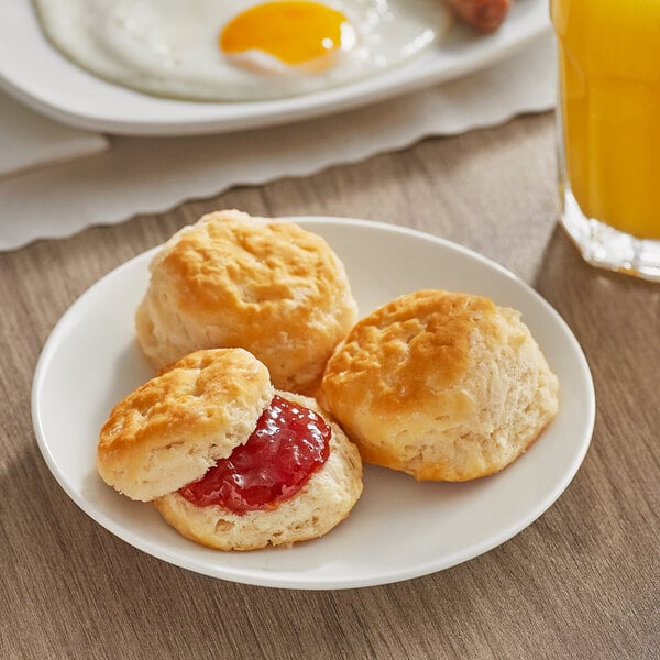 A plate of Bakery Chef whole wheat split buttermilk biscuits with jam and a glass of juice.