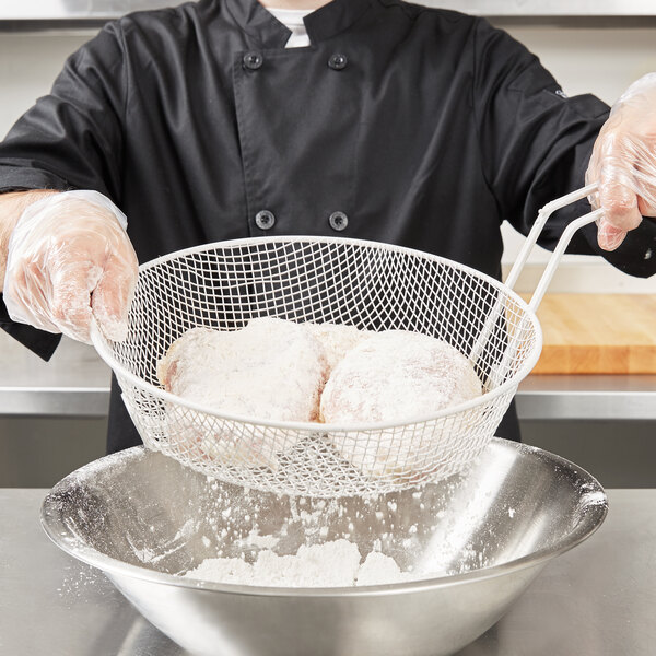 A chef using a white mesh Thunder Group breading basket to coat food.