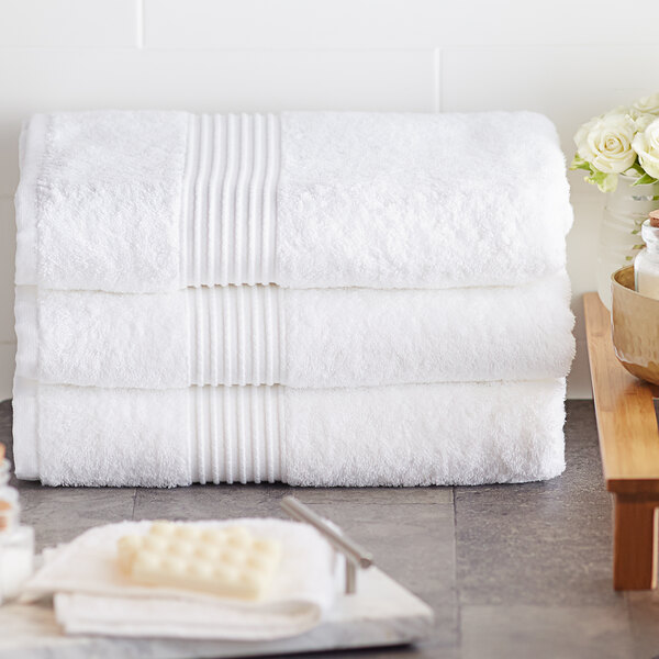 A stack of Lavex Luxury white bath towels on a wood table.
