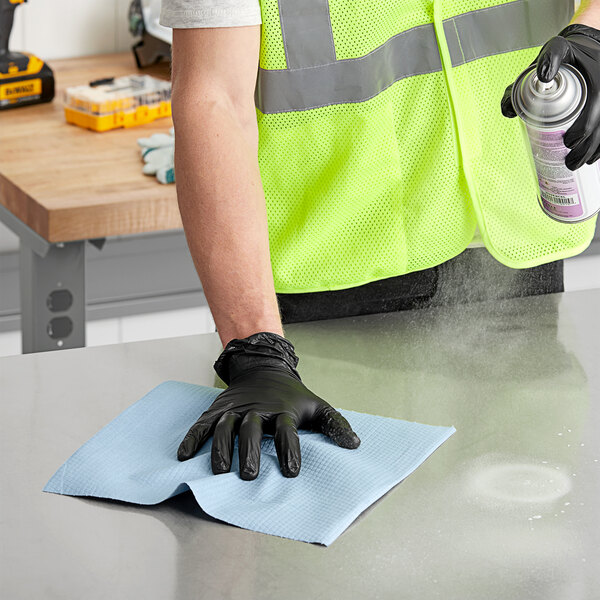 A person wearing black gloves using a Lavex Blue Heavy Weight Industrial Wiper to clean a table.