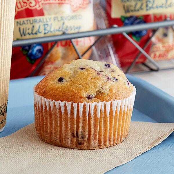 An Otis Spunkmeyer wild blueberry muffin in a paper wrapper on a blue tray.
