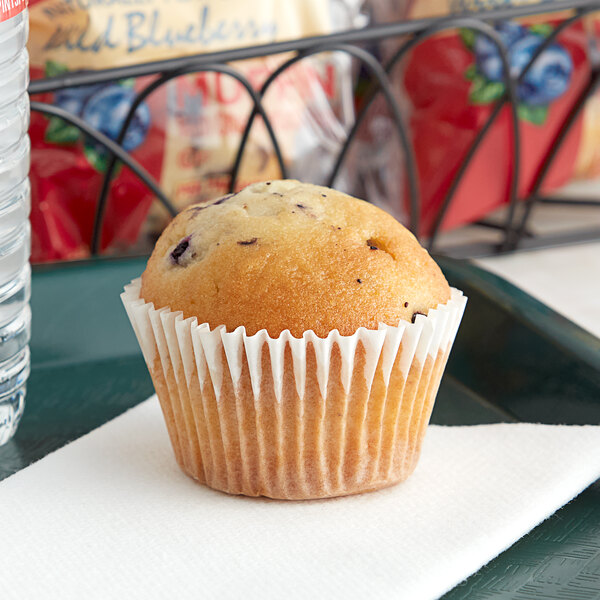 An Otis Spunkmeyer wild blueberry muffin in a paper wrapper on a plate.