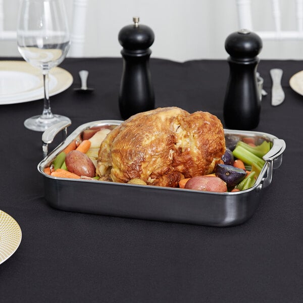 A Vollrath Miramar stainless steel roasting pan with cooked meat and vegetables on a table.