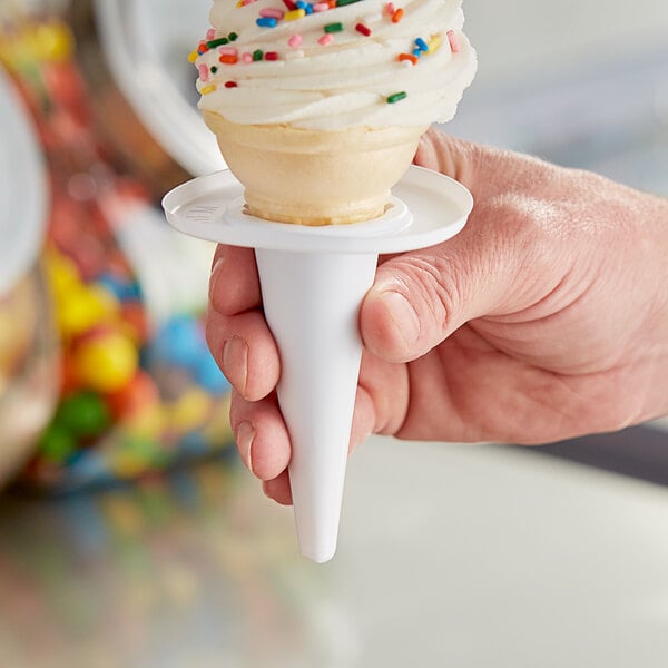 A hand holding a white cone with a vanilla ice cream in it.