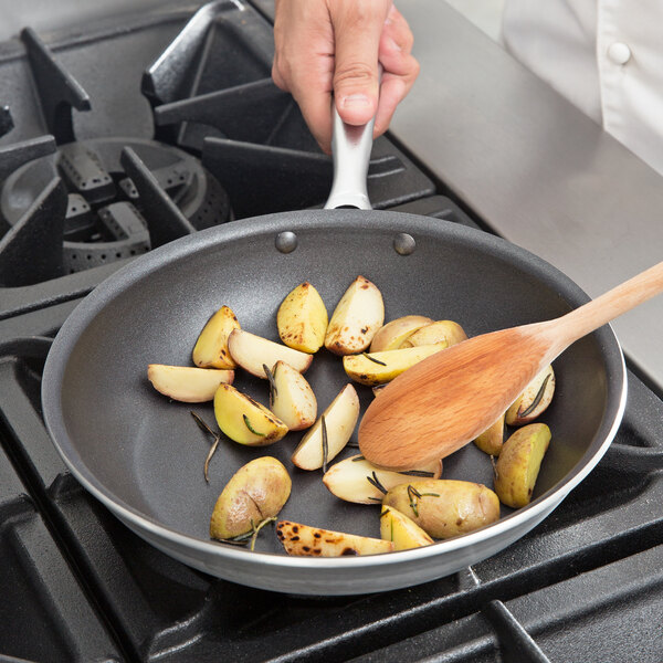A person cooking potatoes in a Vollrath Wear-Ever non-stick fry pan on a stove.