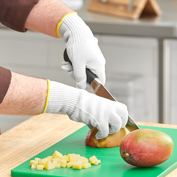 A person wearing Ansell HyFlex cut-resistant gloves cutting a mango on a cutting board.