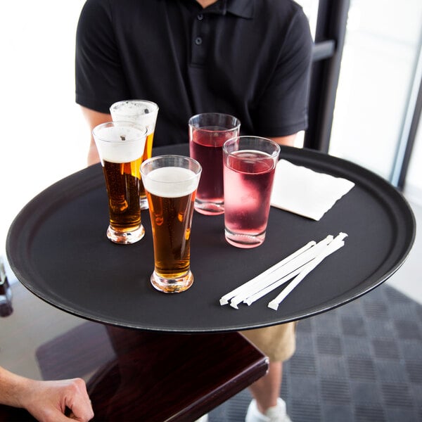 A man in a black shirt holding a Carlisle non-skid oval serving tray with drinks and white straws.