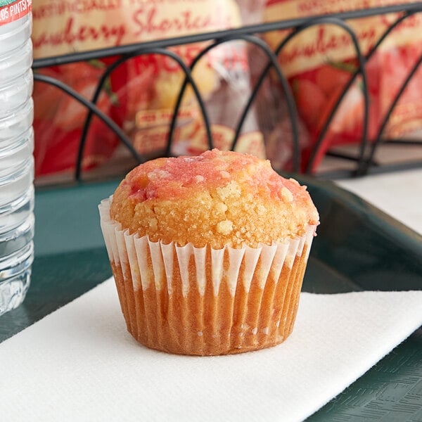 An Otis Spunkmeyer strawberry shortcake muffin with pink frosting on a tray.