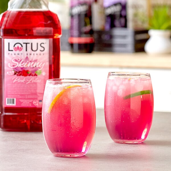 A bottle of Lotus Plant Energy Skinny Pink Lotus concentrate with two glasses of pink liquid with lemon slices.