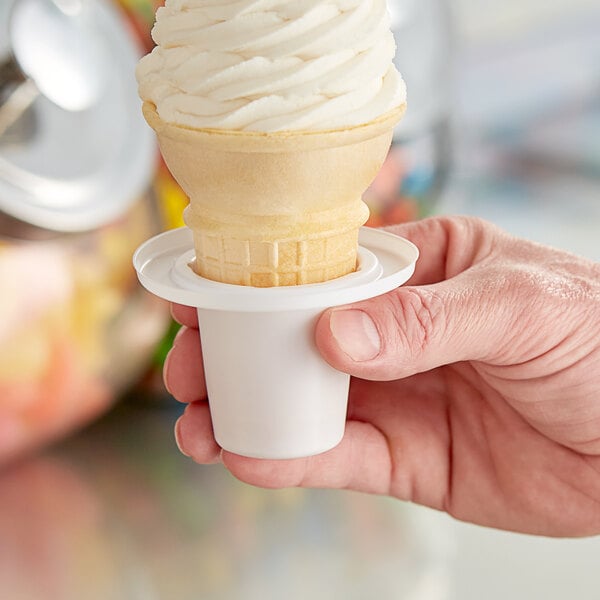 A hand holding a large cup of ice cream with a cone in it.