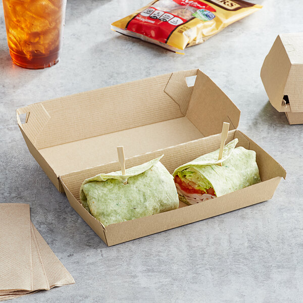 A tortilla wrap and a sandwich in Sabert rectangular kraft take-out boxes on a table with a glass of a drink and ice.