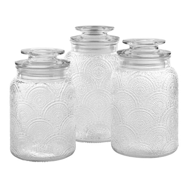 A group of three clear glass canisters with glass lids.