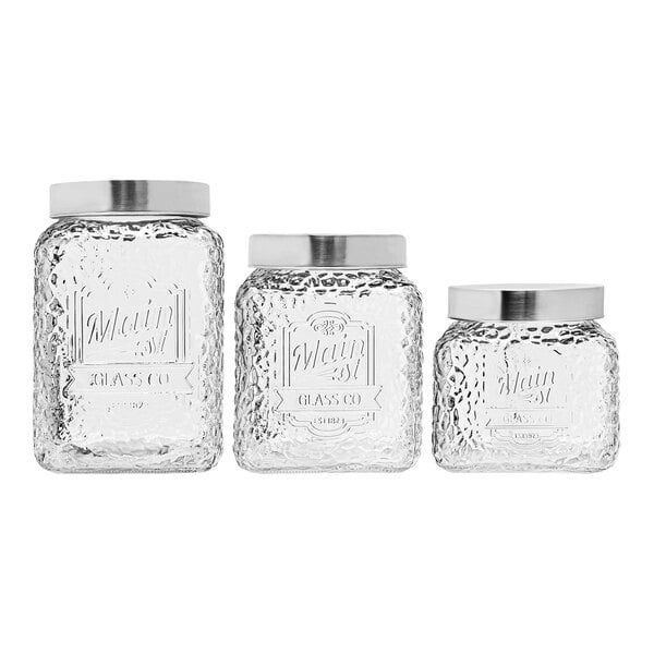 Three clear glass American Atelier Main Street canisters with stainless steel lids.