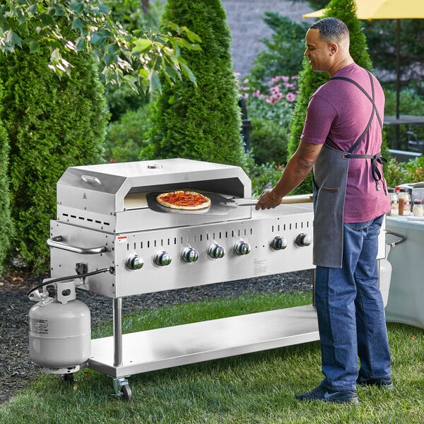 A man wearing an apron cooks a pizza on a Backyard Pro stainless steel grill.
