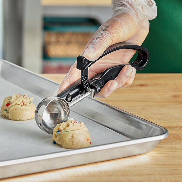 A hand holding a black Choice EZ Grip Squeeze Handle Disher filled with food.