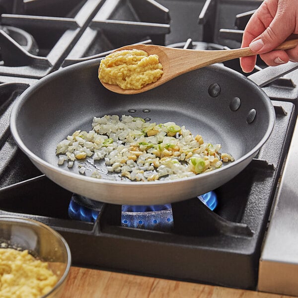 A person stirring food in a frying pan on a stove with a spoon containing SupHerb Farms Ginger Puree.
