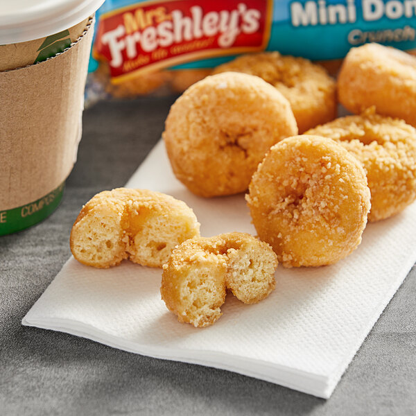 Mrs. Freshley's Crunch Mini Donuts with Coconut Coating on a napkin next to a cup of coffee.