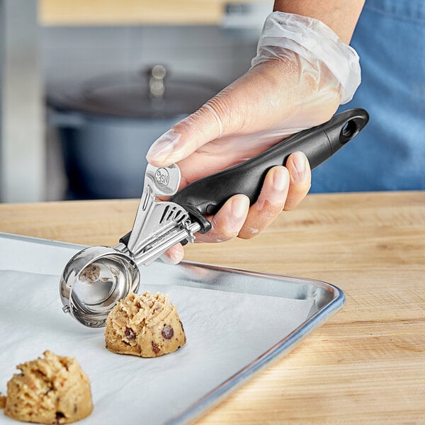 A person using a black-handled metal scoop to make a cookie.