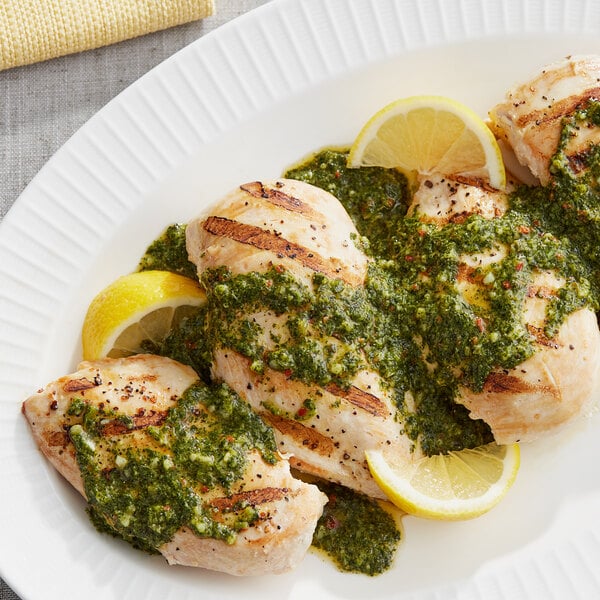 A plate of chicken with Armanino Chimichurri Sauce and lemon wedges.