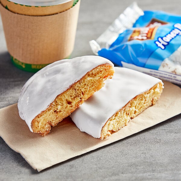 A Mrs. Freshley's Iced Honey Bun with white frosting on a napkin next to a cup of coffee.