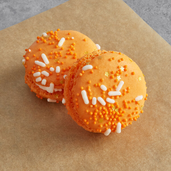 Two orange Macaron Centrale cookies with white sprinkles.