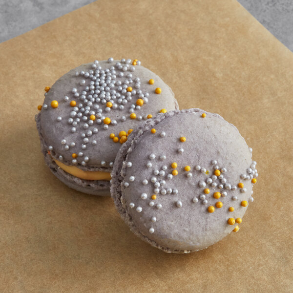 Two Macaron Centrale butterscotch dark chocolate macarons with sprinkles on them on a table in a bakery display.