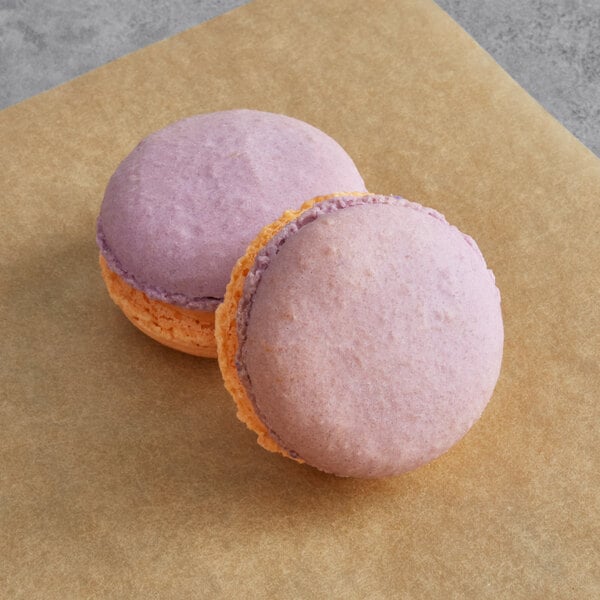 Two blackberry and Thai tea macarons on a table.