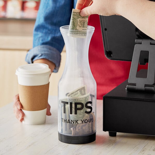 A person putting a dollar bill into a plastic tip jar on a counter.