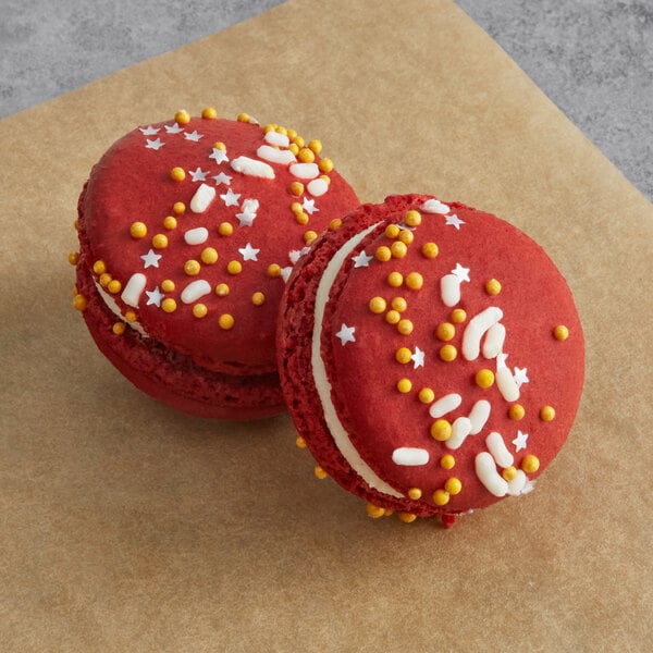 Two red Macaron Centrale macarons with white and yellow sprinkles.