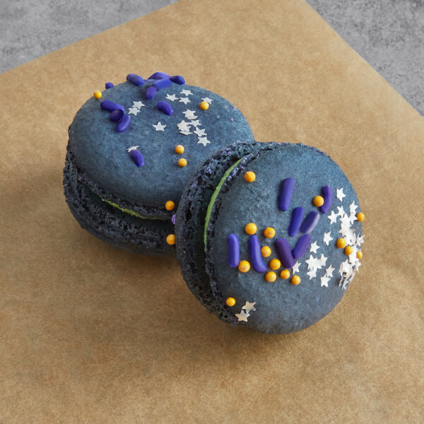 Two blue Macaron Centrale macarons with white and purple sprinkles on top.