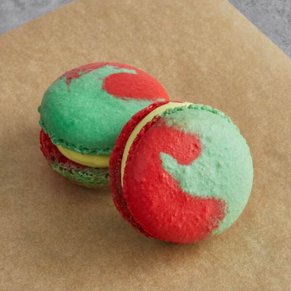 Two colorful Macaron Centrale macarons with green and red icing on a brown surface.