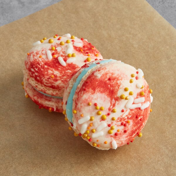Two Macaron Centrale white chocolate macarons with sprinkles on top on a brown paper bag.