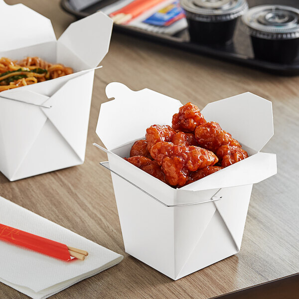 Two Emperor's Select white paper take-out boxes with food in them on a table.