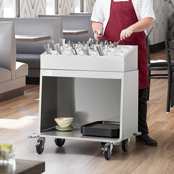 A man in a red apron standing by a ServIt flatware cart with utensils in it.