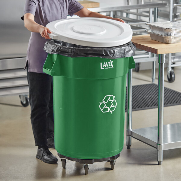 A woman standing next to a Lavex green recycling can with a white lid.