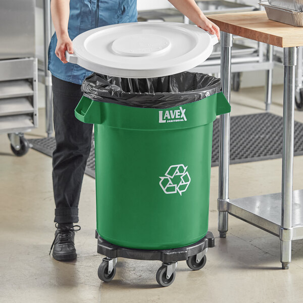 A woman putting a white lid on a green Lavex recycling can.