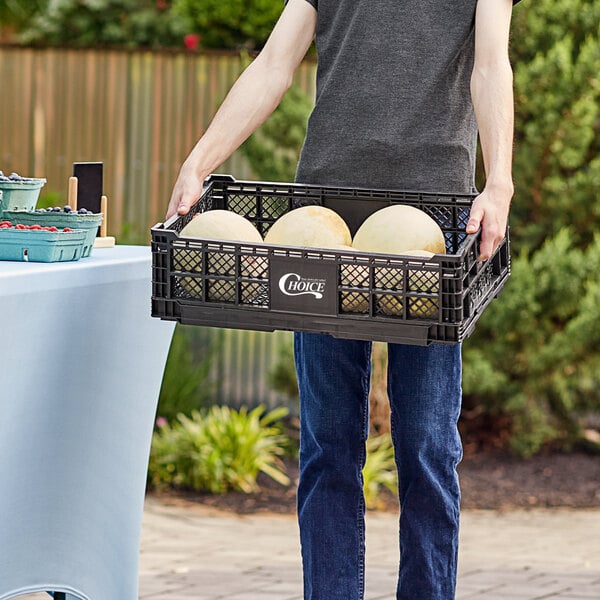 A man holding a black vented Choice crate of melons.