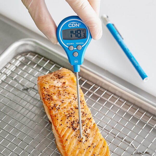 A person using a blue CDN digital pocket probe thermometer to check the temperature of salmon.